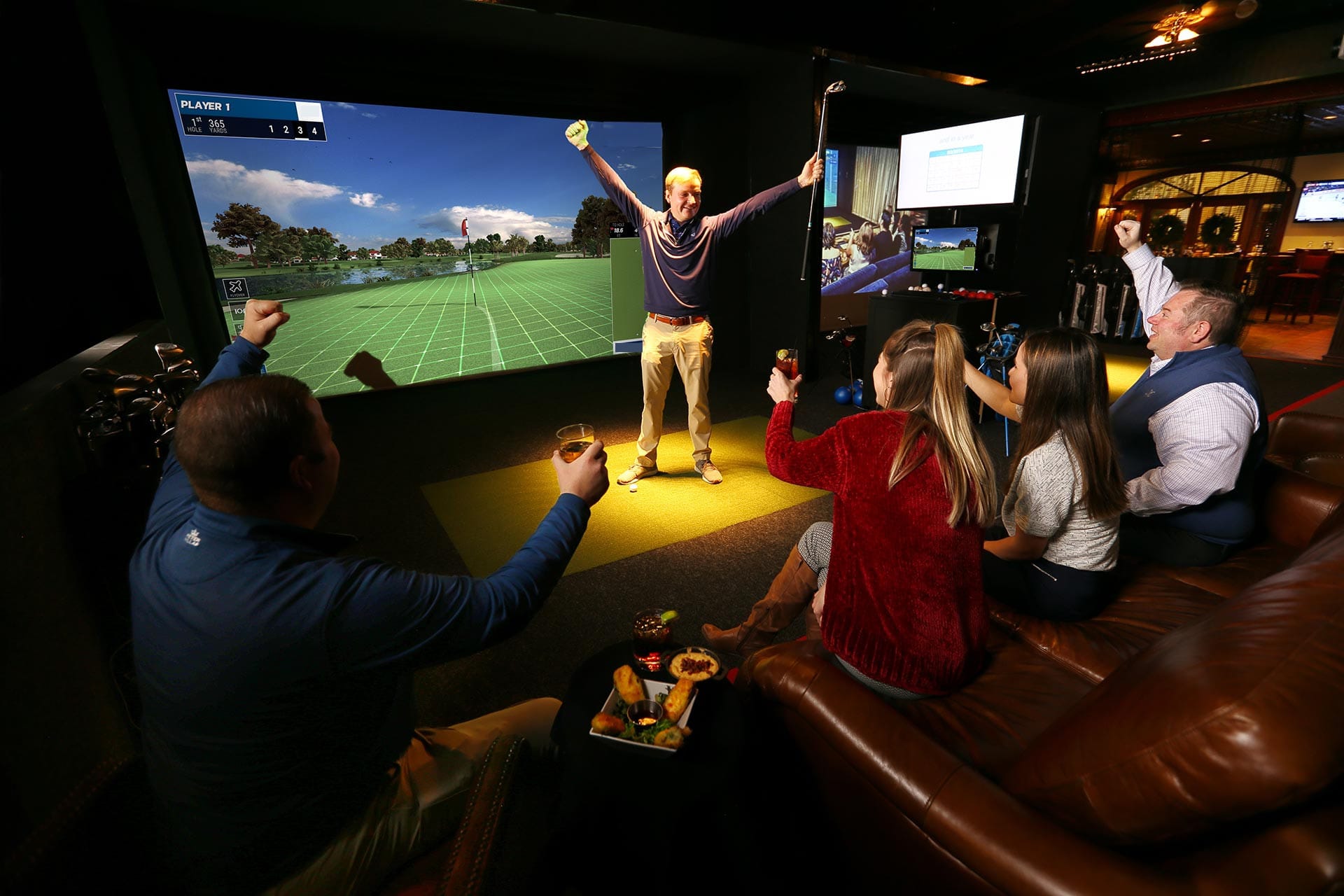 Six friends in a simulator lounge cheering as one of them raises his arms after a shot